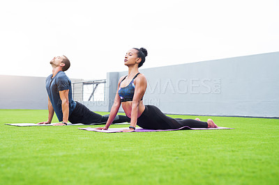 Buy stock photo Shot of a young man and woman practising yoga together outdoors