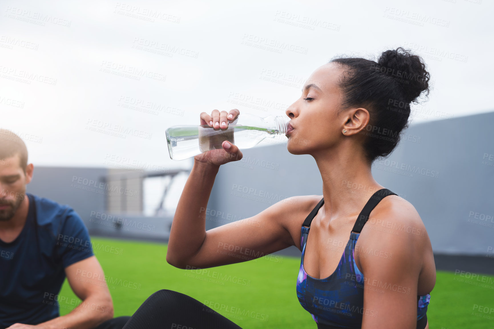 Buy stock photo Shot of a young woman drinking water while exercising with her partner outdoors