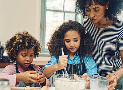 Buy stock photo Cropped shot of two young children baking at home with the help of their mother