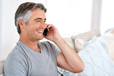Buy stock photo Cropped shot of a handsome mature man sitting on his living room sofa alone and talking on his cellphone
