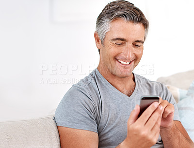 Buy stock photo Cropped shot of a handsome mature man sitting on his living room sofa and using his cellphone during the day