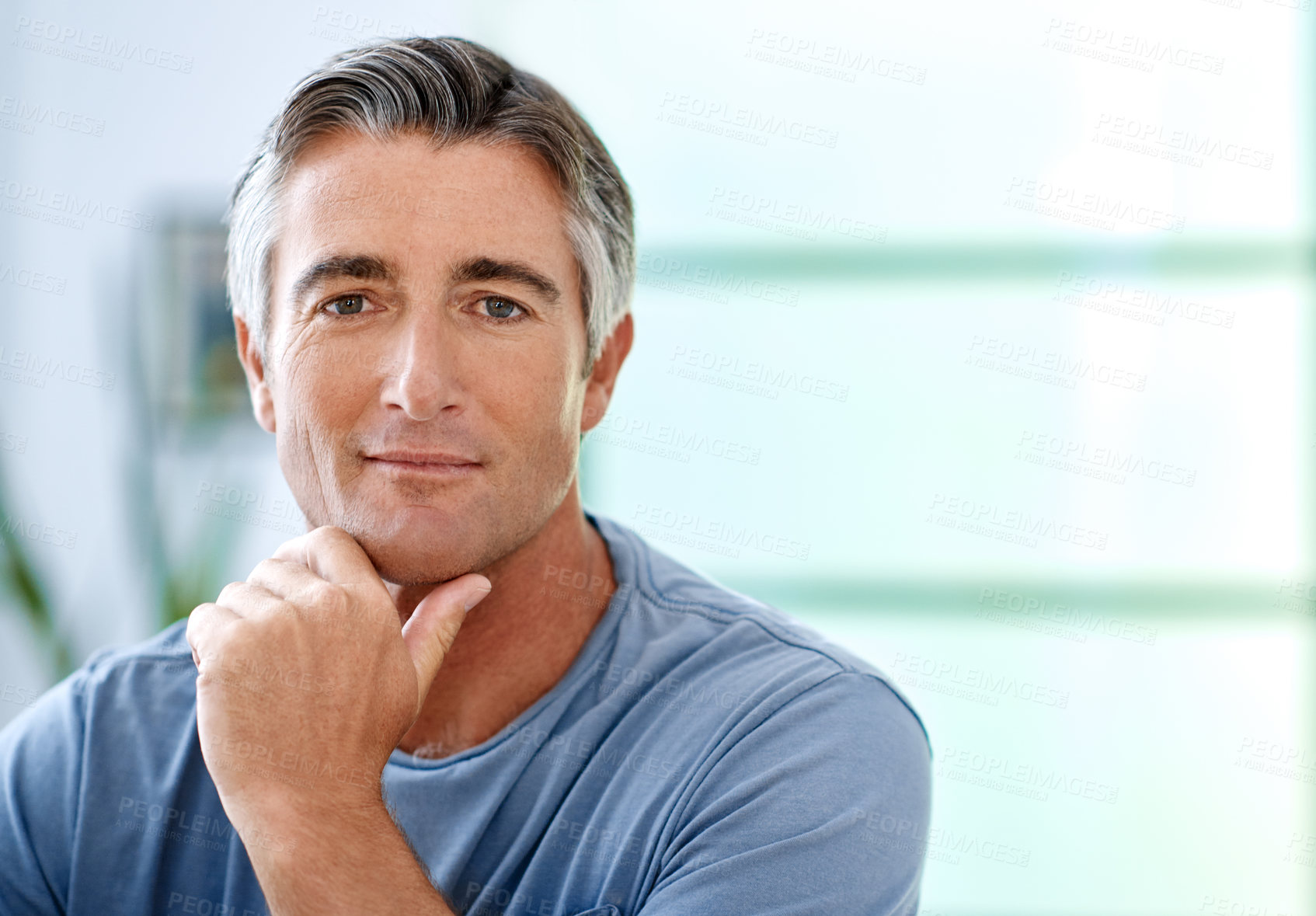 Buy stock photo Cropped portrait of a handsome mature man sitting with his hand on his chin while indoors in his house