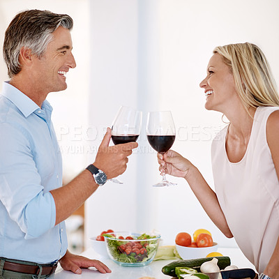 Buy stock photo Cropped shot of an affectionate mature couple toasting with red wine while making dinner