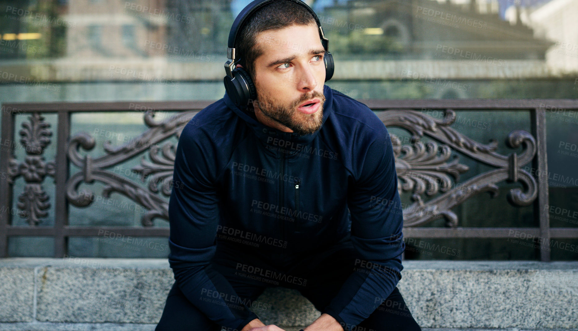Buy stock photo Shot of a young man listening to music during a break from his workout in the city