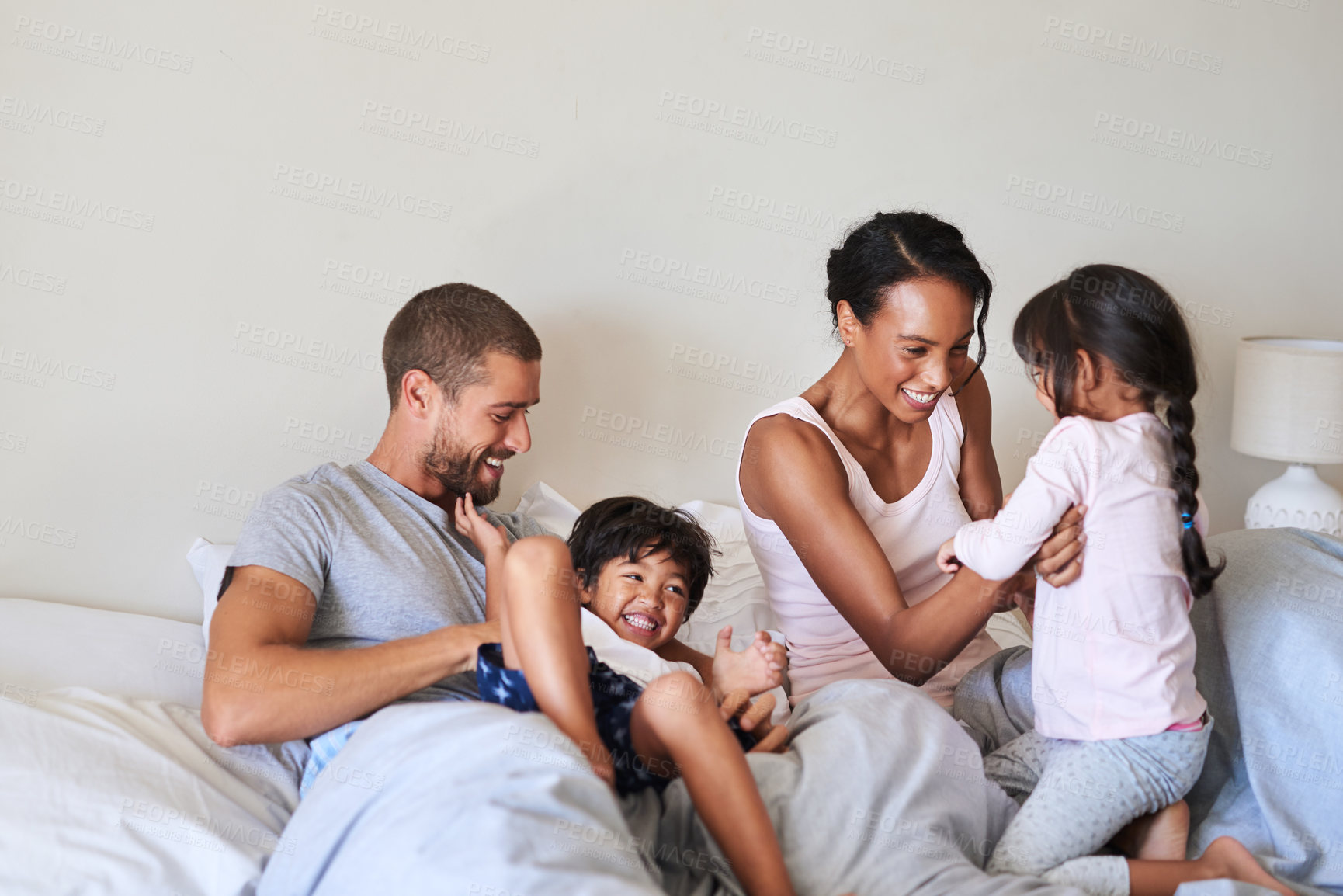 Buy stock photo Mom, dad and children in bedroom for playing, bonding and happy relationship in morning. Family, childhood and mother, father and kids tickle for laughing, fun and relax on bed together in home