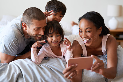 Buy stock photo Shot of a beautiful young family of four taking a selfie with a  cellphone in their bedroom at home