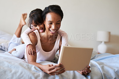 Buy stock photo Shot of a beautiful young mother and daughter using a digital tablet while relaxing in bed together at home