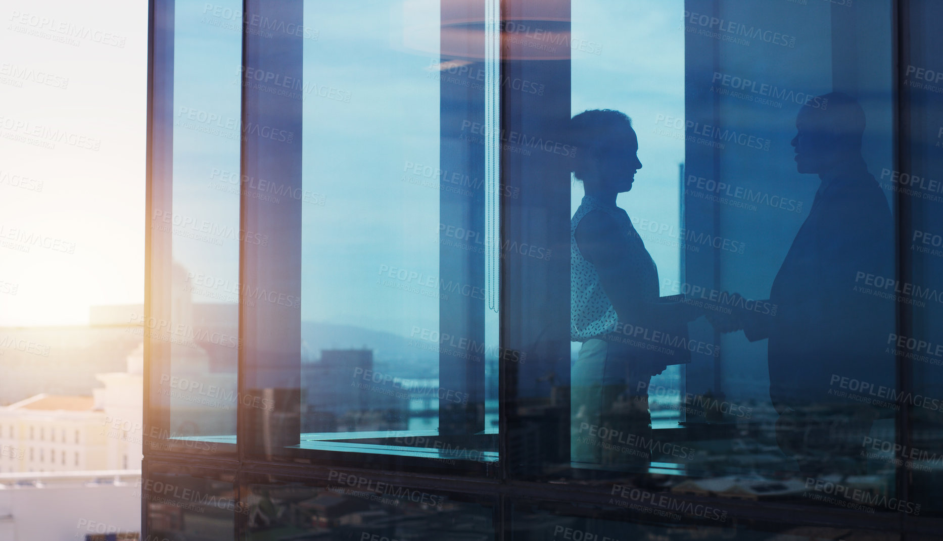 Buy stock photo Silhouette shot of two businesspeople shaking hands inside an office building