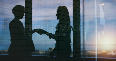 Buy stock photo Silhouette shot of two businesspeople shaking hands inside an office building