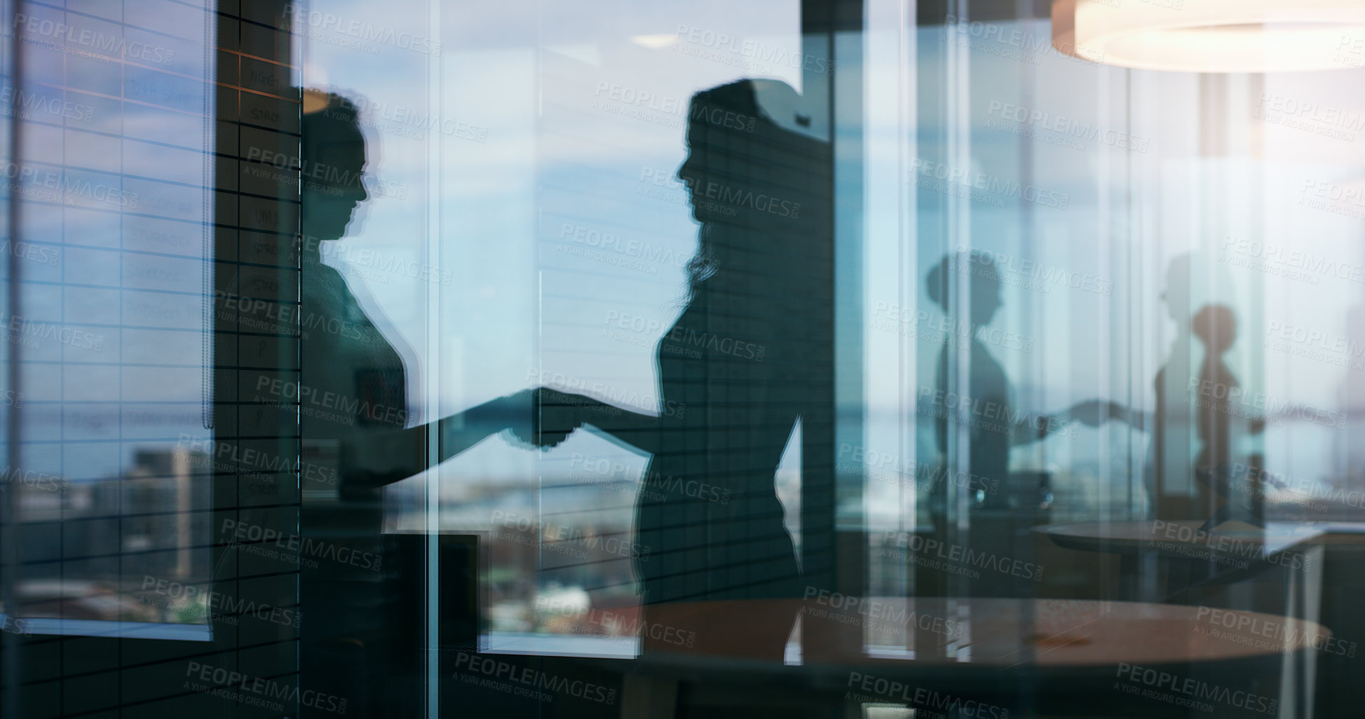 Buy stock photo Silhouette shot of two businesspeople shaking hands inside an office building