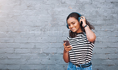 Buy stock photo Shot of a young woman using a cellphone while wearing headphones against a grey wall