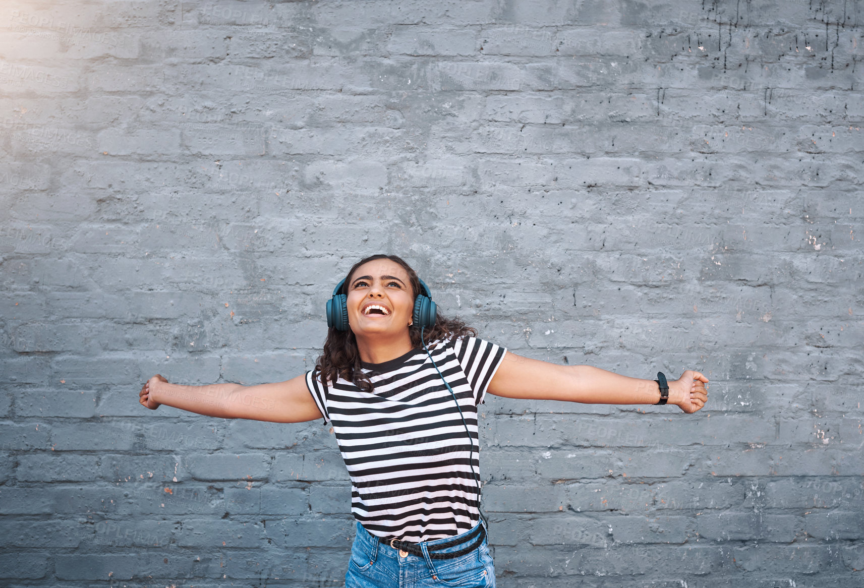 Buy stock photo Happy, excited and girl with headphones, streaming music and smile on grey wall with mindset, joyful and cheerful. Person, outdoor and headset for radio, listening to audio and sound with freedom