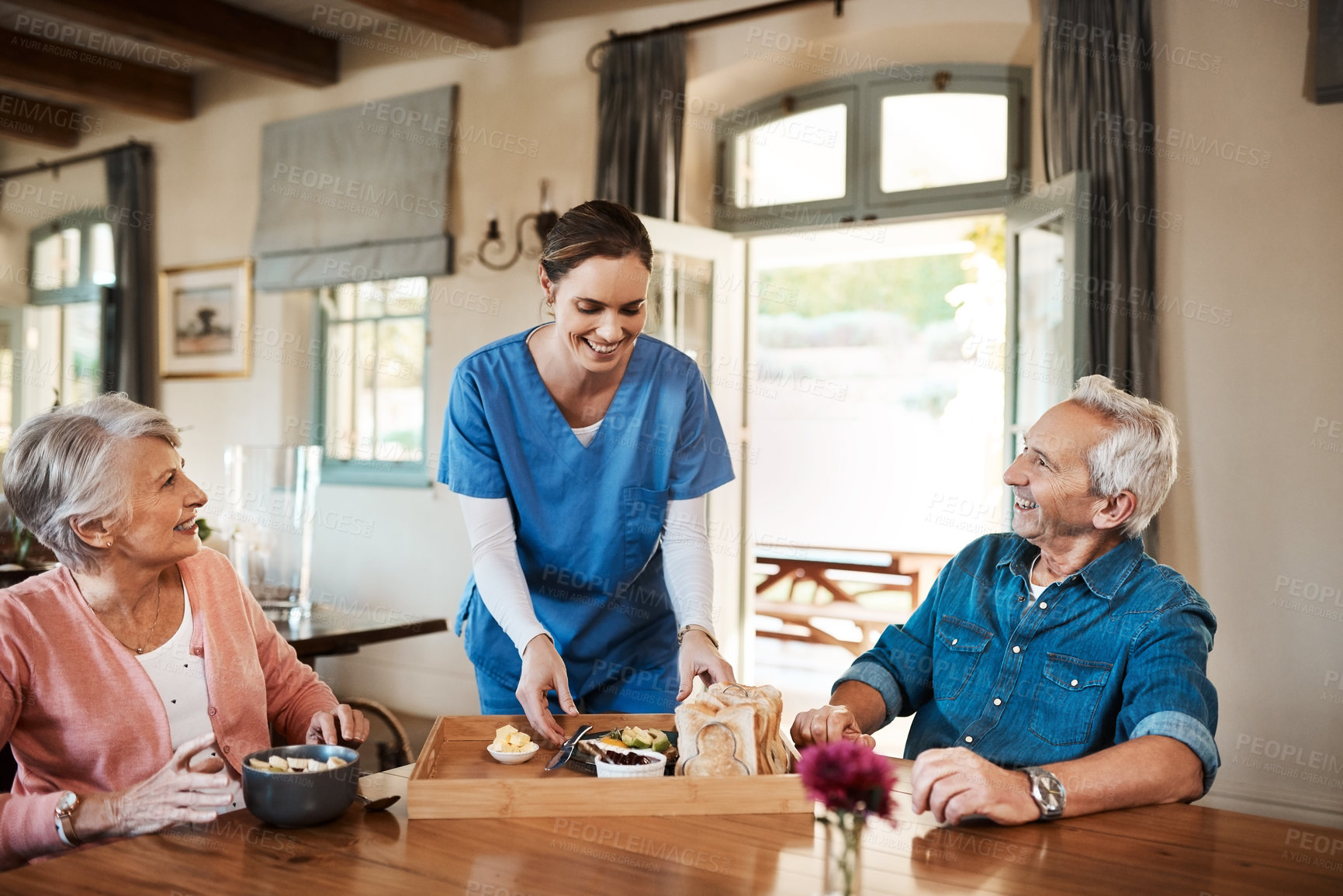 Buy stock photo Shot of a young nurse checking up on a senior couple during breakfast at a nursing home