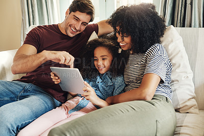 Buy stock photo Shot of a beautiful young family of three using a digital tablet while relaxing on a couch together at home
