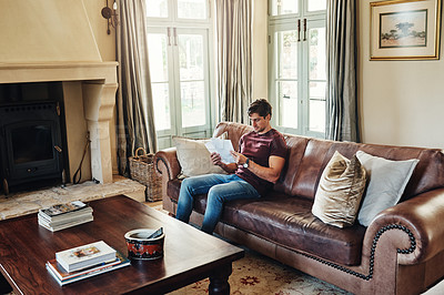 Buy stock photo Full length shot of a handsome young man going over some paperwork while relaxing on a couch at home