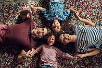 Buy stock photo High angle shot of a beautiful young family lying down on a carpet and holding hands together at home