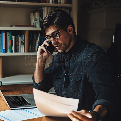 Buy stock photo Shot of a handsome young businessman making a phone call while working in his office at home