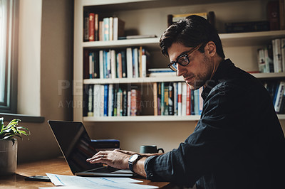 Buy stock photo Shot of a handsome young businessman working on a laptop in his office at home