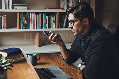 Buy stock photo Shot of a handsome young businessman using a cellphone while working in his office at home