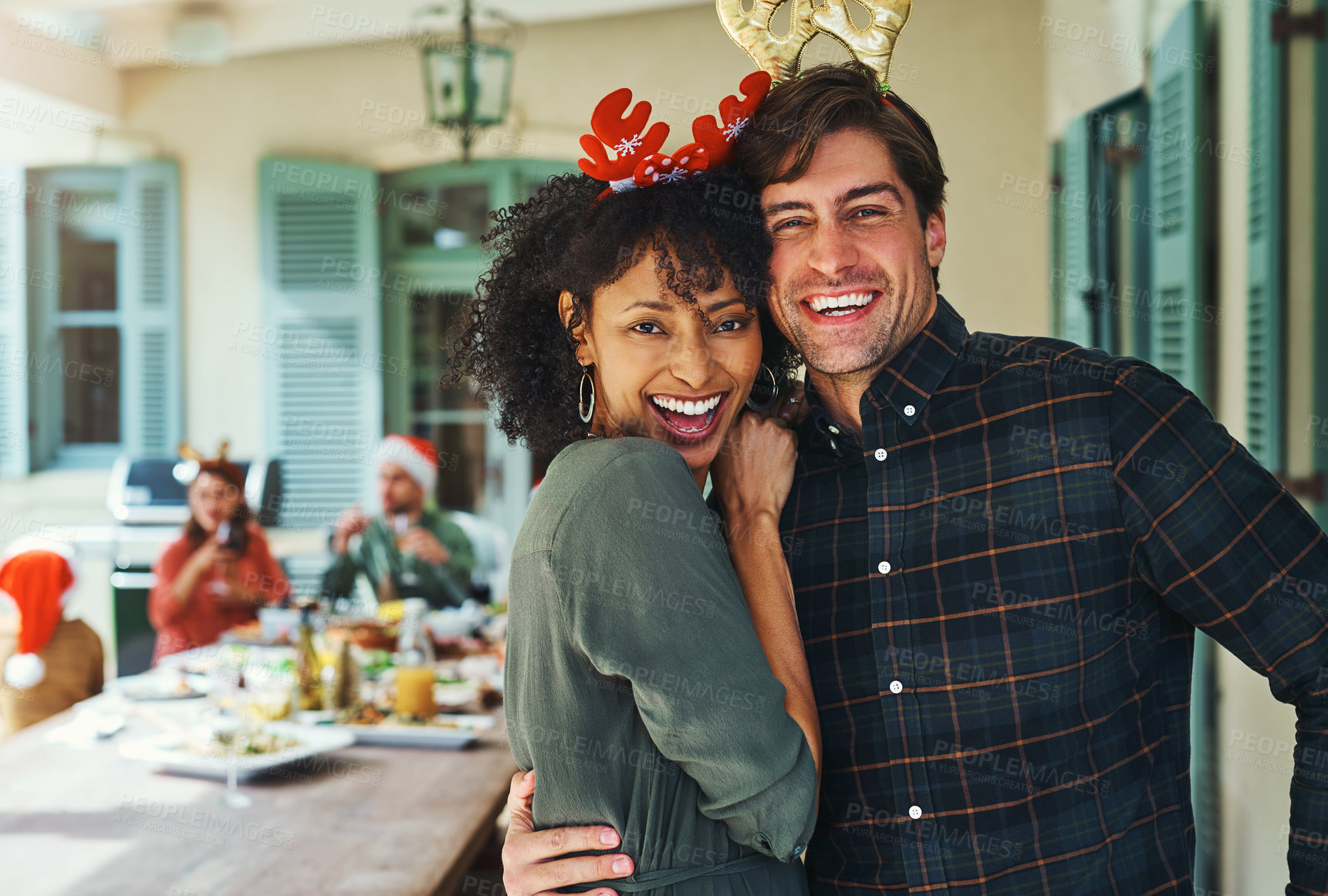 Buy stock photo Portrait of a happy young couple celebrating Christmas together over lunch with friends and family in the background