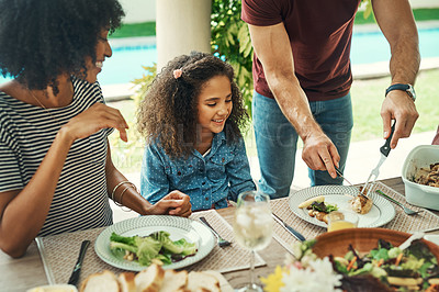 Buy stock photo Shot of an adorable little girl enjoying a meal with her parents outdoors