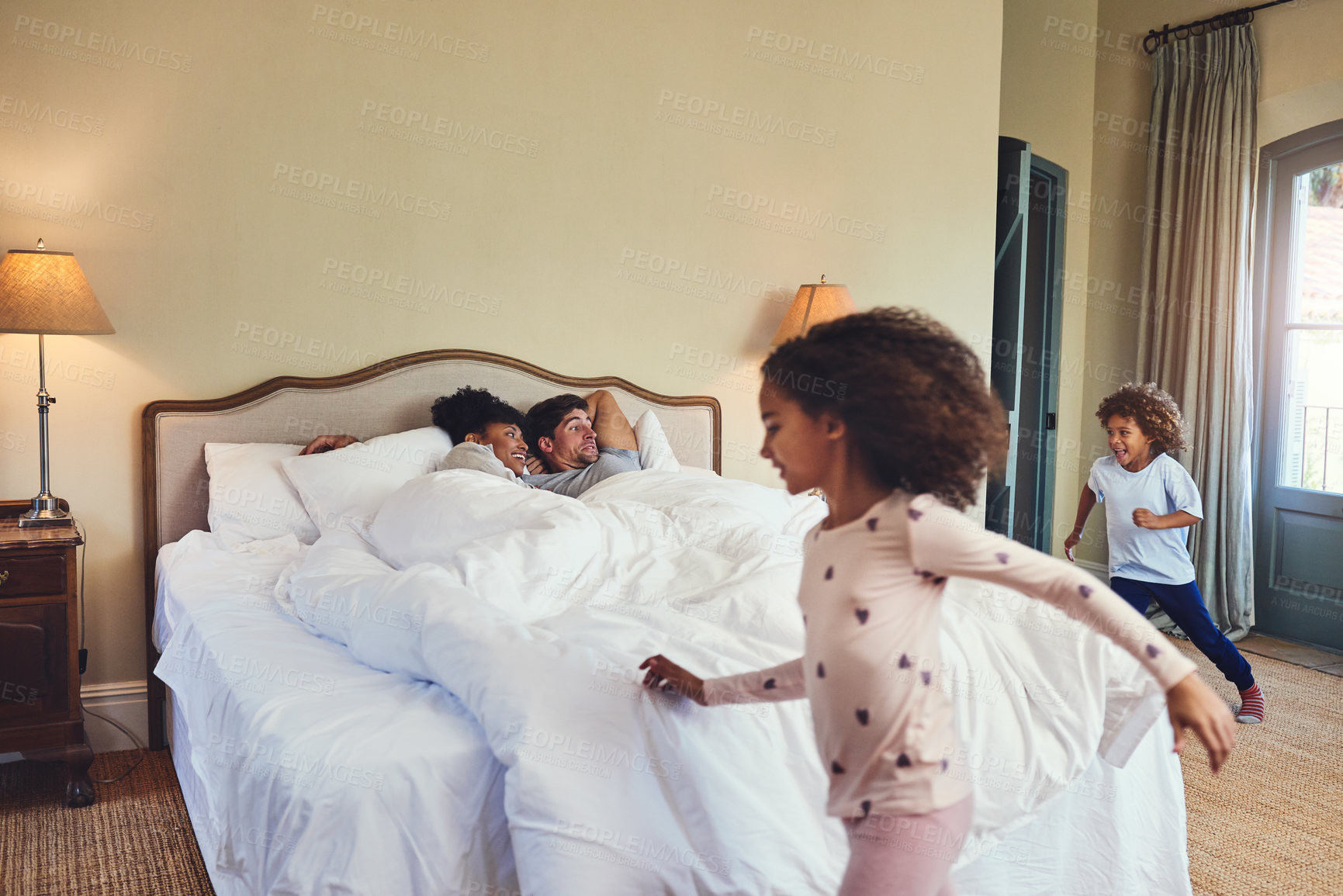 Buy stock photo Excited, parents and children running in bedroom with energy, noise or waking up family for holiday or vacation in hotel. Happy people, mom or dad with morning surprise, laugh and carefree kids in UK