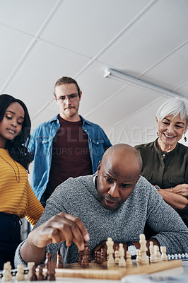 Buy stock photo Shot of a mature businessman playing chess in his office with his colleagues rooting and watching in the background