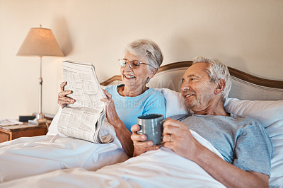 Buy stock photo Cropped shot of a senior woman reading a newspaper in bed while her husband drinks a cup of coffee