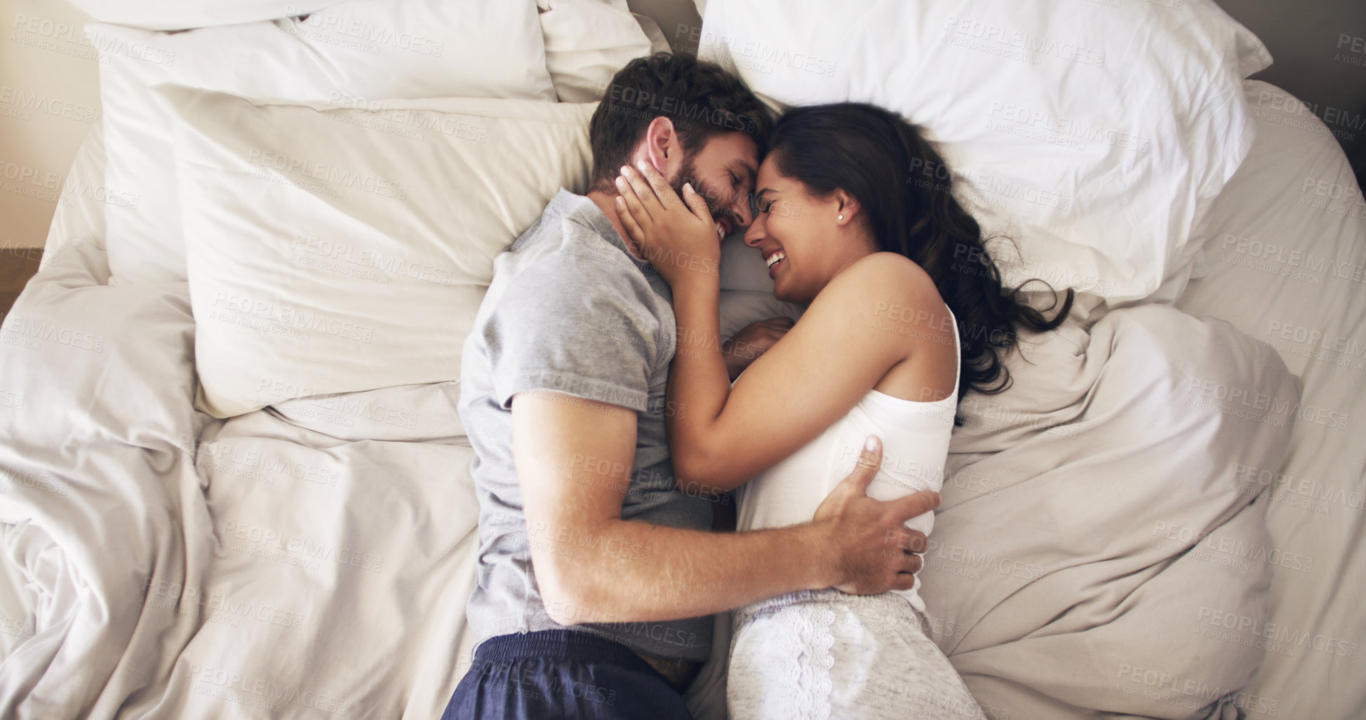 Buy stock photo Shot of an affectionate young couple embracing in bed at home