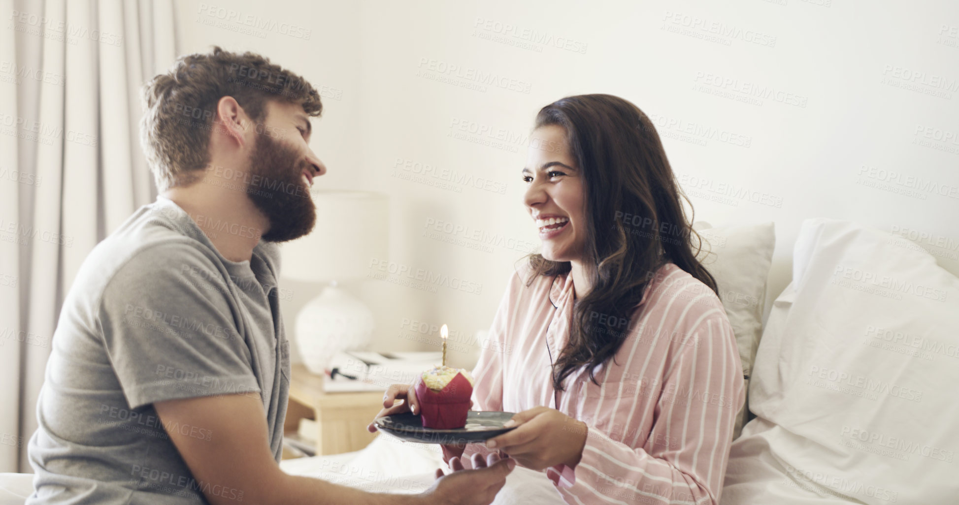 Buy stock photo Shot of a young man surprising his wife with a cupcake in bed at home