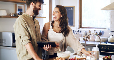 Buy stock photo Shot of a young couple using a digital tablet while preparing breakfast at home