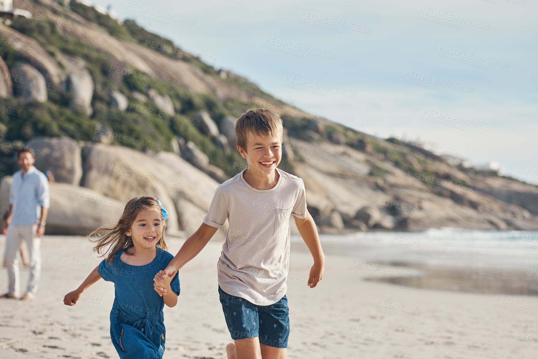 Buy stock photo Cropped shot of a happy young boy holding his little sister's hand and running along the beach with her