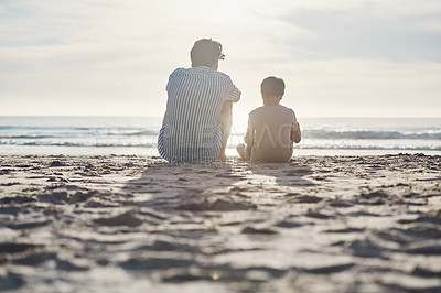 Buy stock photo Rearview shot of an unrecognizable father sitting and bonding with his son during an enjoyable day on the beach