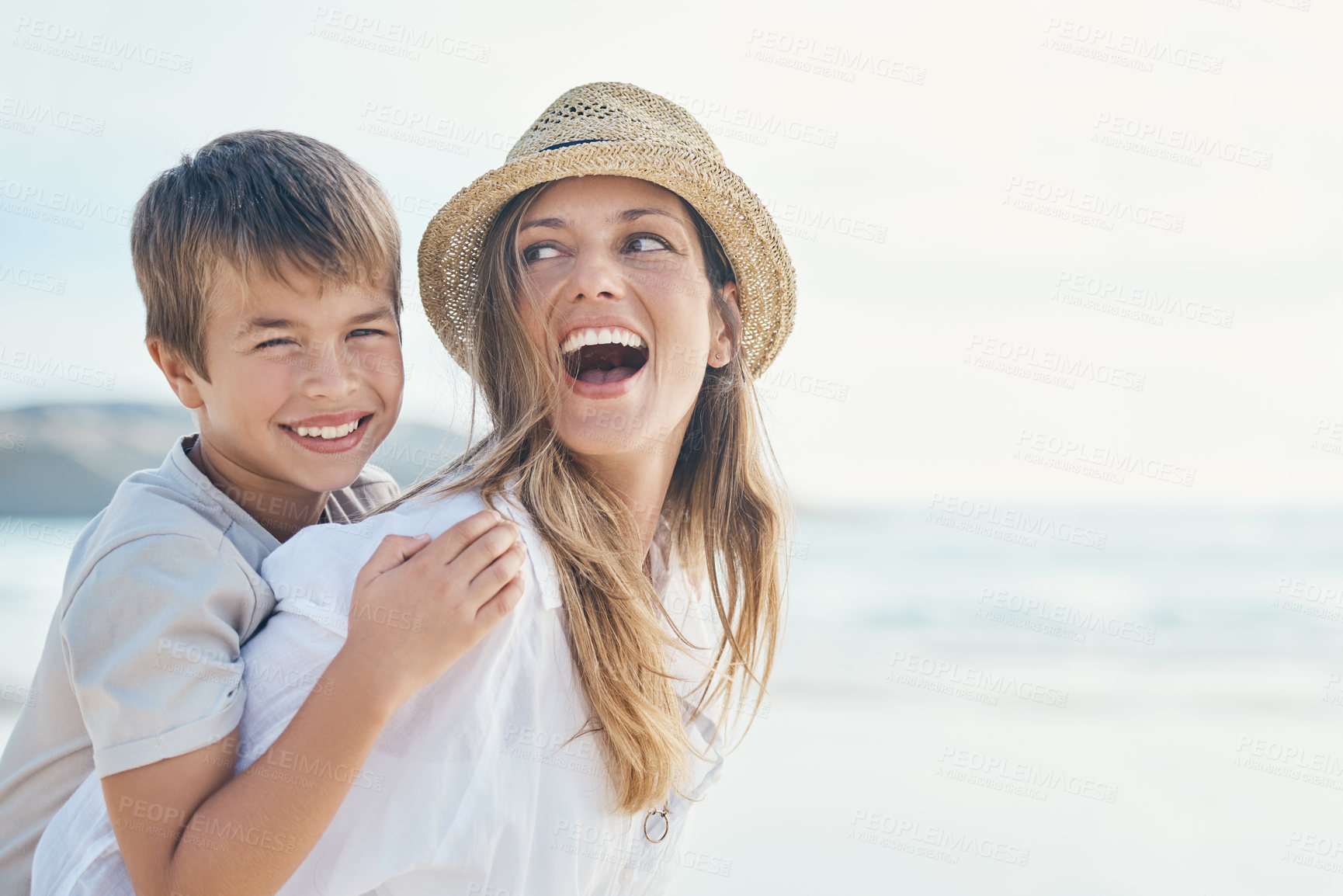 Buy stock photo Cropped shot of an attractive young mother bonding with her son and giving him a piggyback ride on the beach