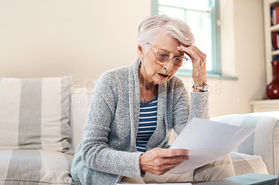 Buy stock photo Shot of a senior woman looking stressed while going through paperwork at home