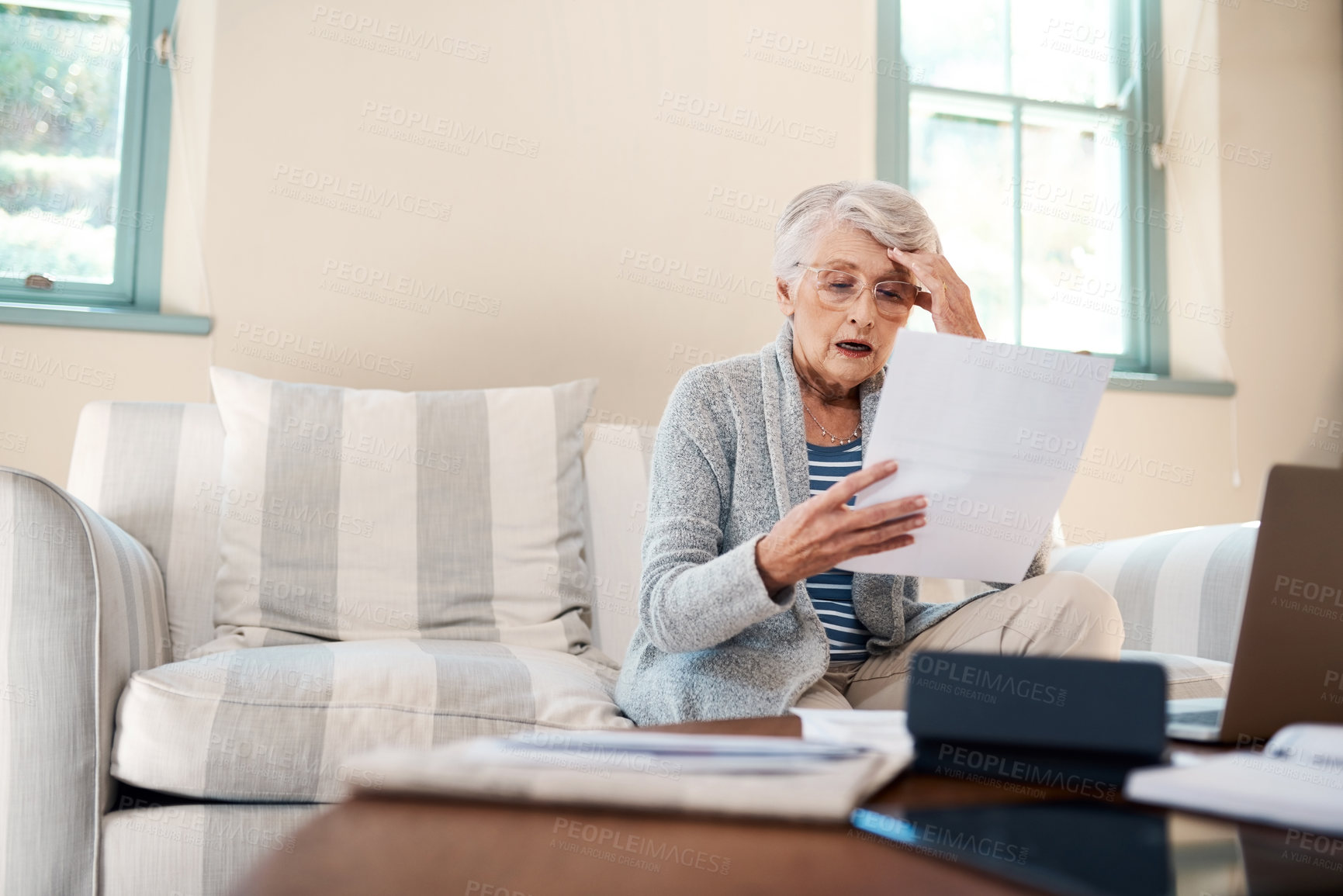 Buy stock photo Shot of a senior woman looking shocked while going through paperwork at home