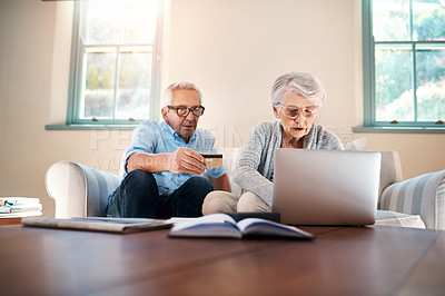 Buy stock photo Shot of a senior couple using a credit card while going through paperwork at home