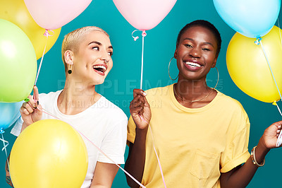 Buy stock photo Studio shot of two young women holding a bunch of colourful balloons against a turquoise background