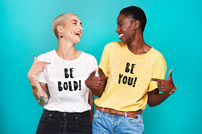 Buy stock photo Studio shot of two confident young women pointing at their statement t shirts against a turquoise background
