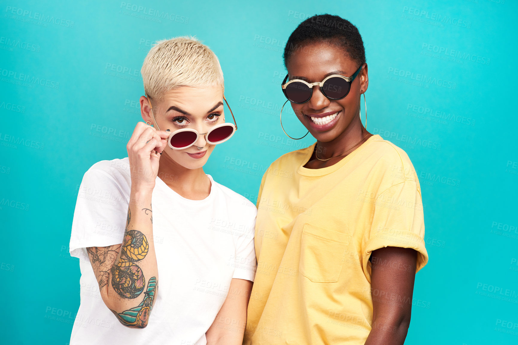 Buy stock photo Studio shot of two young women wearing sunglasses against a turquoise background