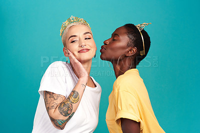 Buy stock photo Studio shot of two young women wearing crowns and kissing against a turquoise background
