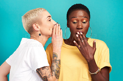 Buy stock photo Studio shot of a young woman whispering in her friend’s ear against a turquoise background