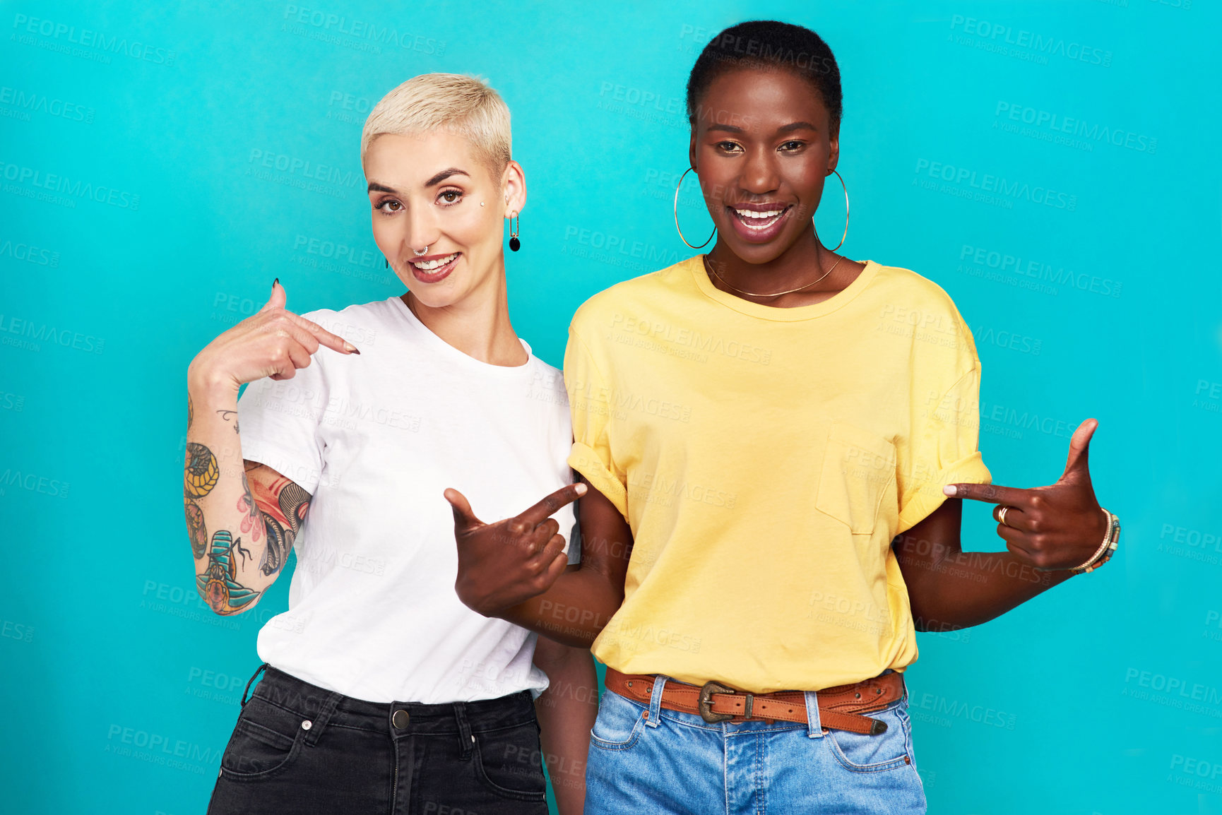 Buy stock photo Studio shot of two confident young women pointing at their t shirts against a turquoise background
