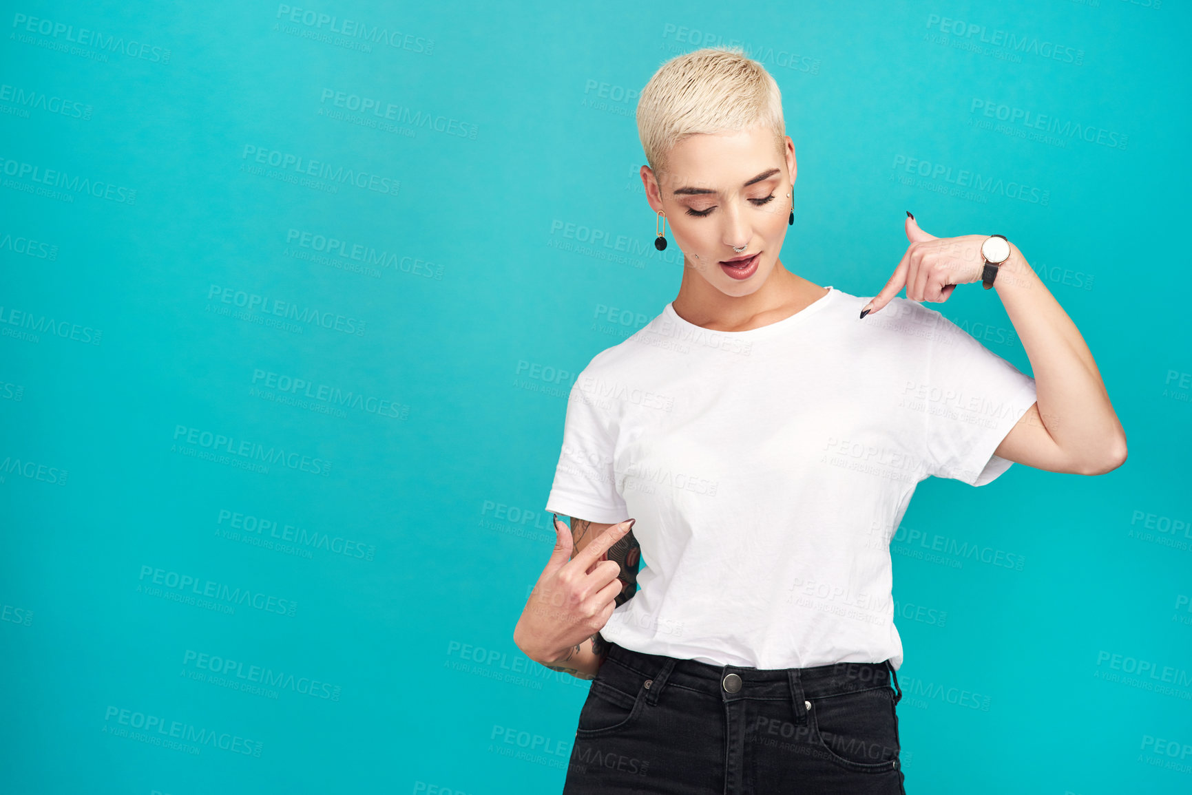 Buy stock photo Studio shot of a confident young woman pointing at her t shirt against a turquoise background