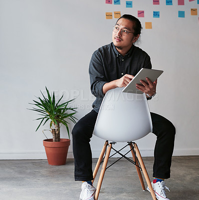 Buy stock photo Full length shot of a creative young businessman sitting on a chair and using his digital tablet at work