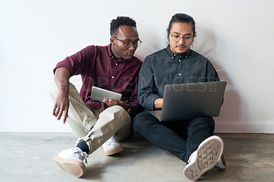 Buy stock photo Full length shot of two young businessmen sitting in the floor and using their digital devices together at work