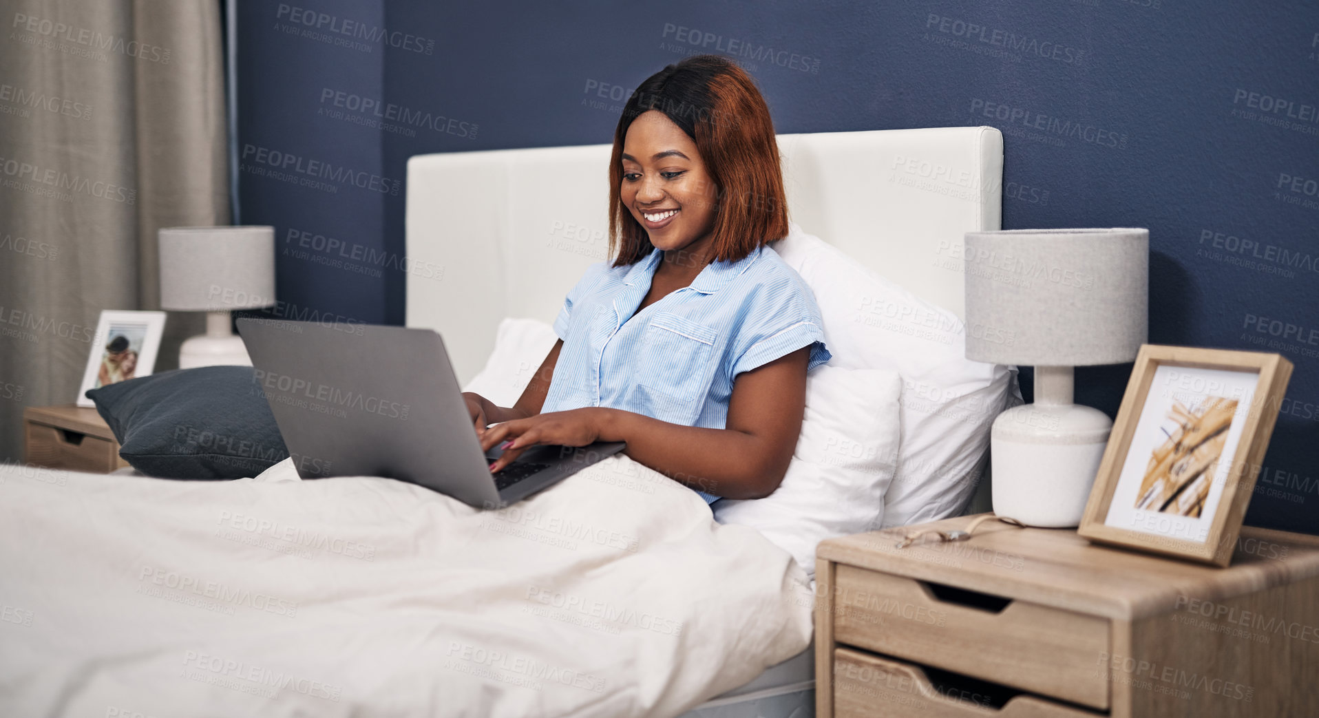Buy stock photo Cropped shot of an attractive young woman using her laptop while sitting in bed