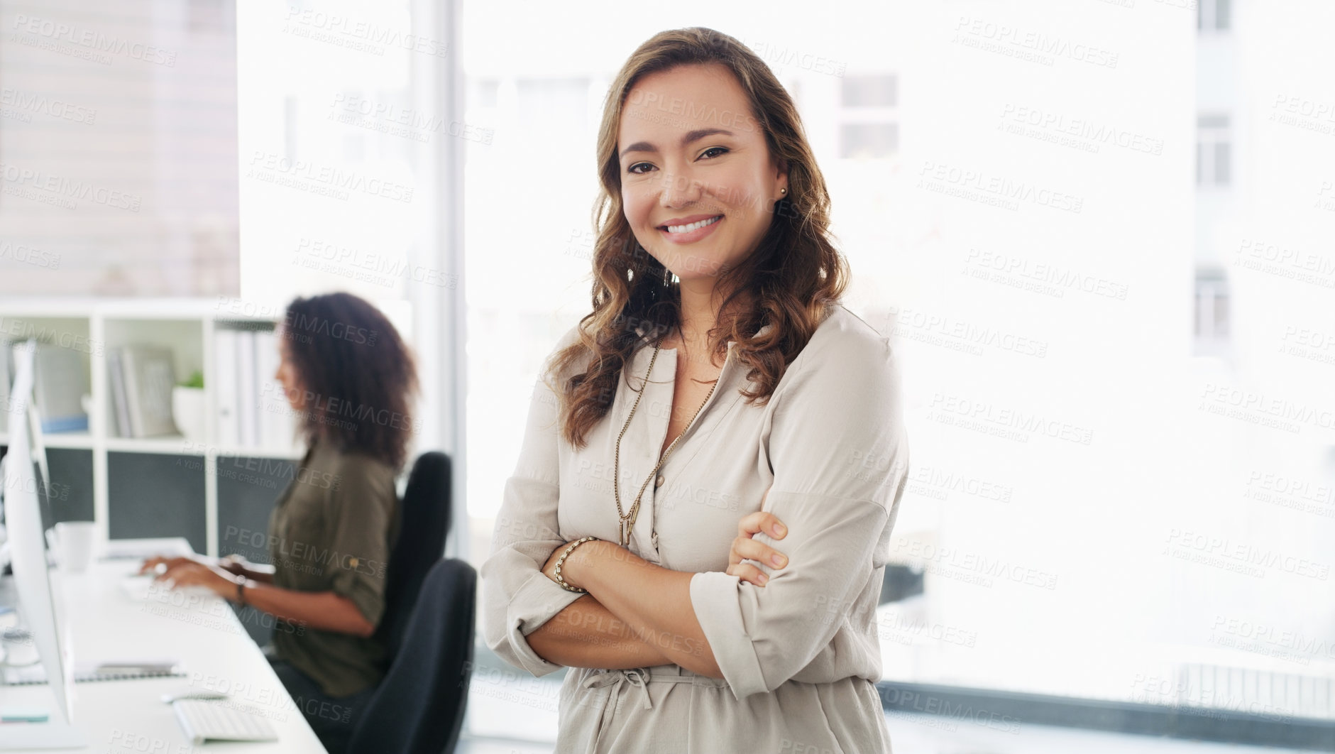 Buy stock photo Portrait of a confident young businesswoman working in a modern office with her colleague in the background