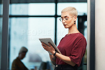 Buy stock photo Cropped shot of an attractive young businesswoman wearing spectacles and using a tablet while standing alone in her office