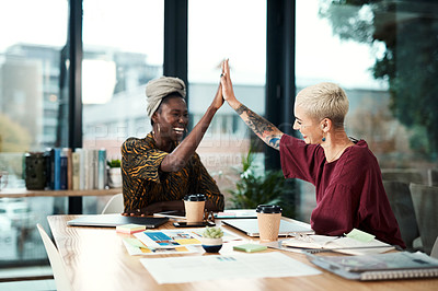 Buy stock photo Cropped shot of two attractive young businesswomen sitting in the office and giving each other a high five